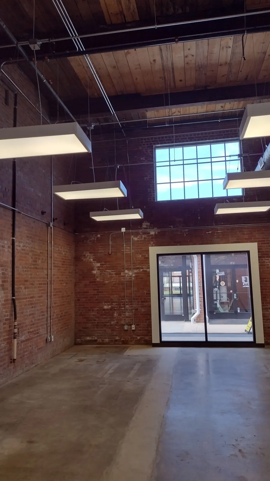 Office suite at Drayton Mills with exposed brick, heart-pine ceiling and tall mill windows onto the Marketplace