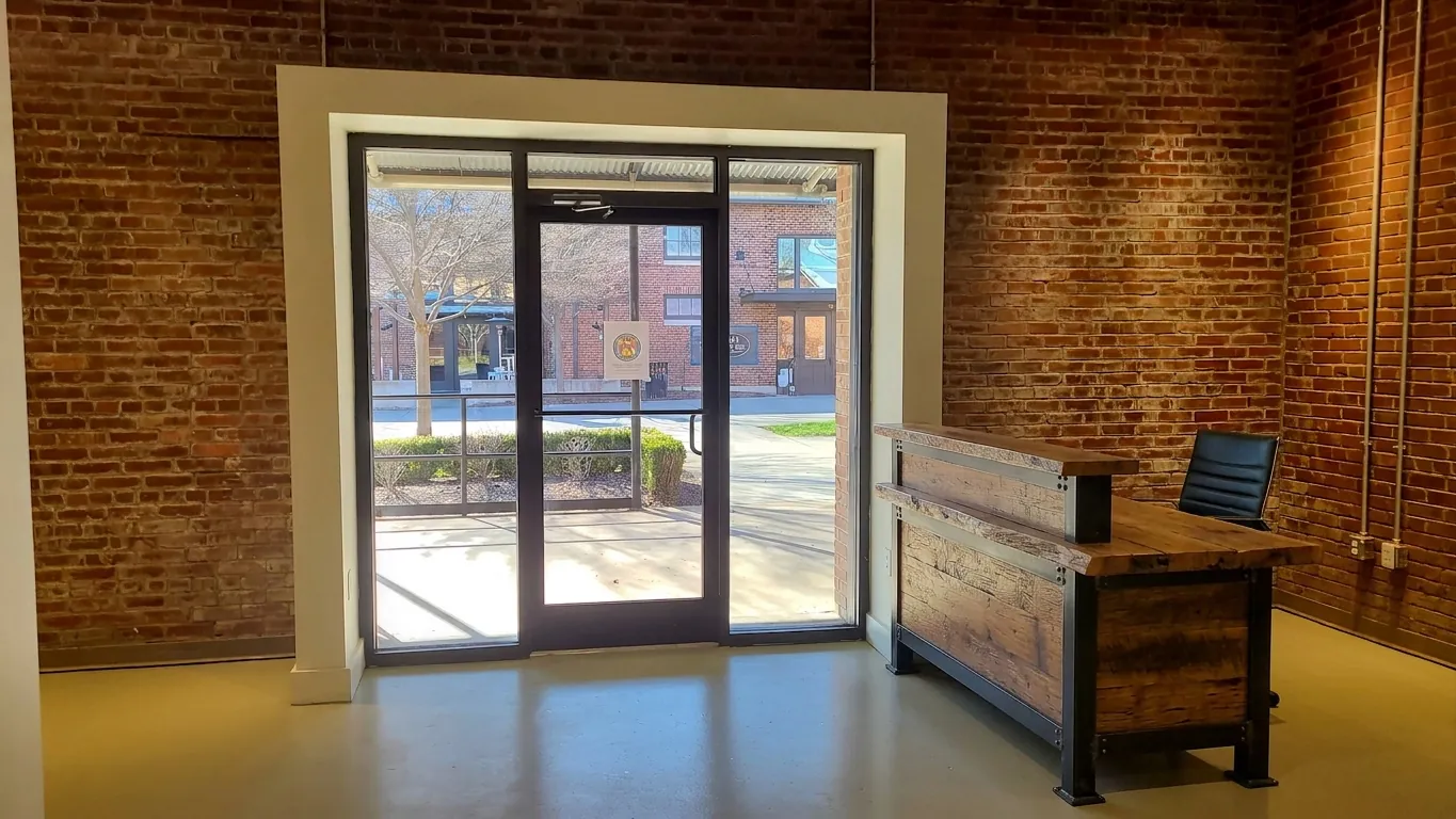 Suite 120C at Drayton Mills: exposed brick walls and a storefront glass entry onto the Marketplace walk
