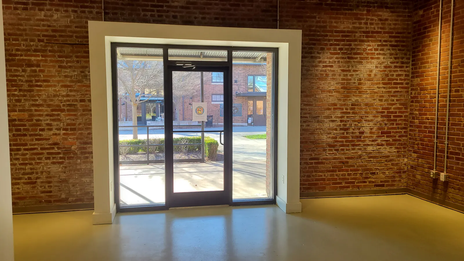 Storefront glass door framed in exposed brick, looking out to the Marketplace walk